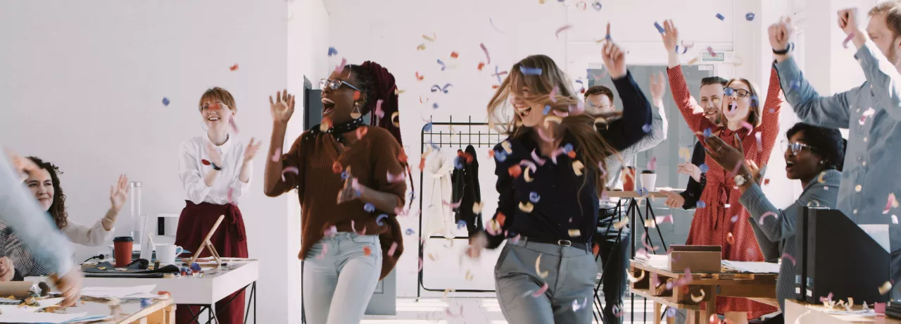 A team celebrating at work with confetti falling down in the background 
