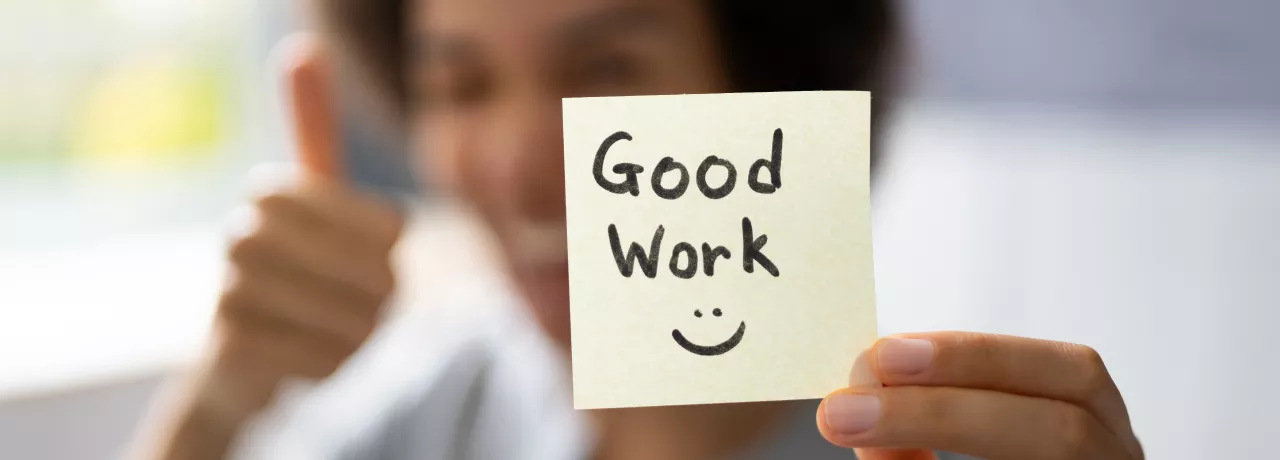 A woman holding a sticky note that says "Good work" with a smiley face 