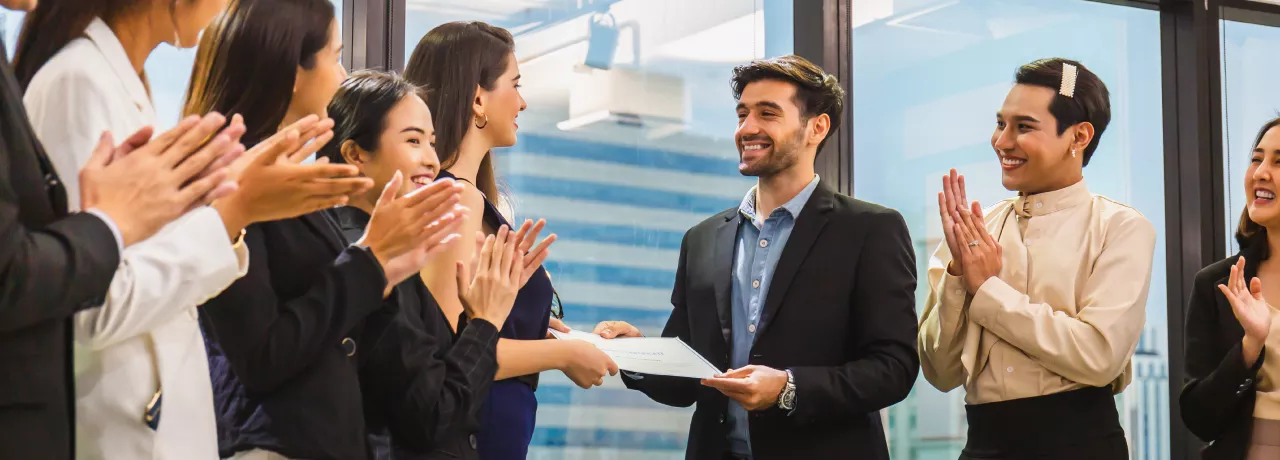 Image shows an employee receiving a certificate in front of a group of employees. 