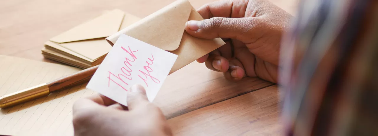 Image shows a person putting a note that says "thank you" into an envelope 
