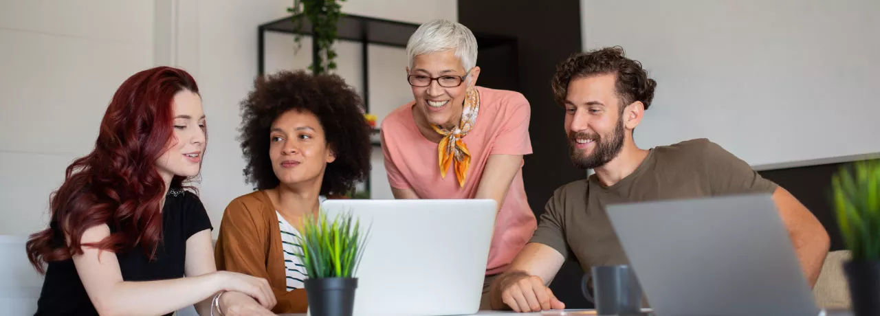 Four employees in varying generations working together at a computer at work. 