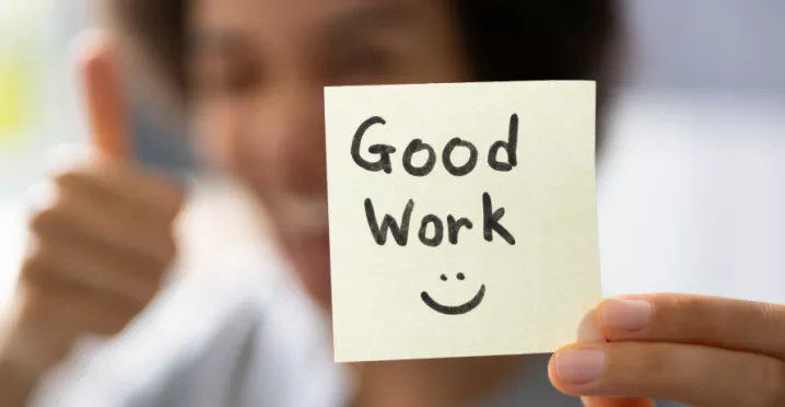 A woman holding a sticky note that says "Good work" with a smiley face