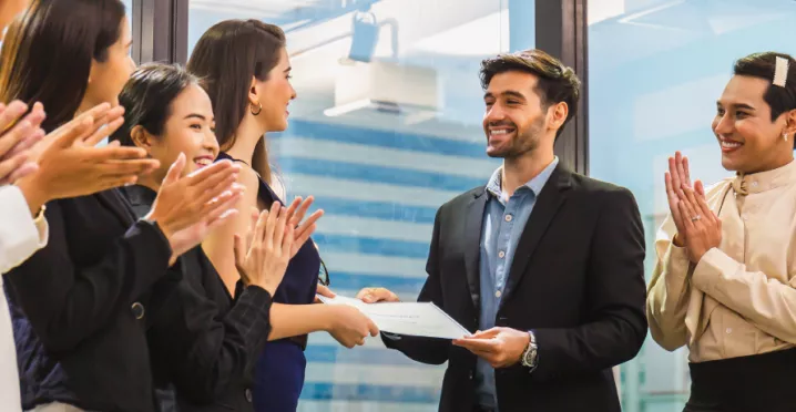 Image shows an employee receiving a certificate in front of a group of employees.