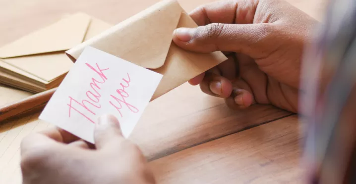 Image shows a person putting a note that says "thank you" into an envelope