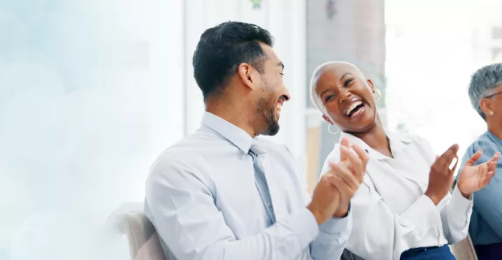 Image shows two employees laughing together along with two others in the background.