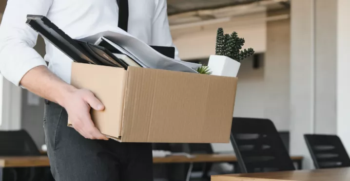 Image shows a person leaving an office with a box of items.
