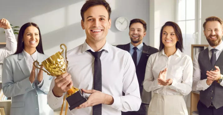 An employee holding an award trophy in front of their colleagues