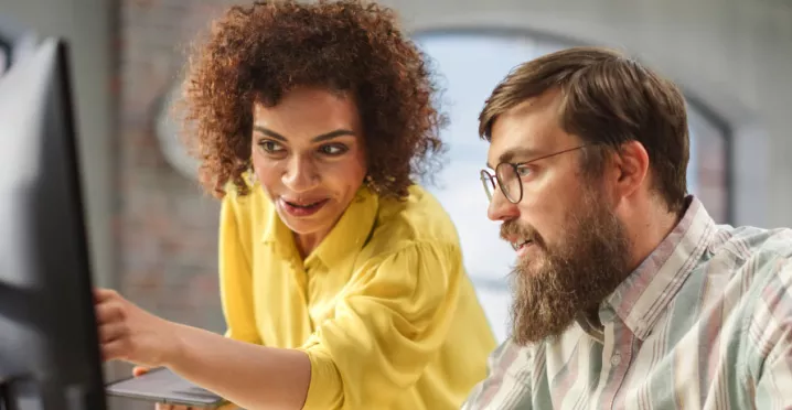 An employee training a new hire in front of a computer as part of their onboarding strategy