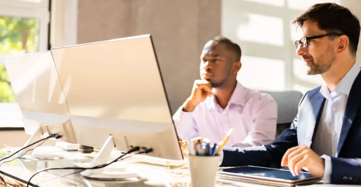 Two employees happily looking at a computer screen at their desk
