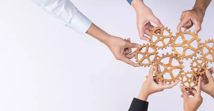 A group of employees creating a cogwheel with each holding a small cog