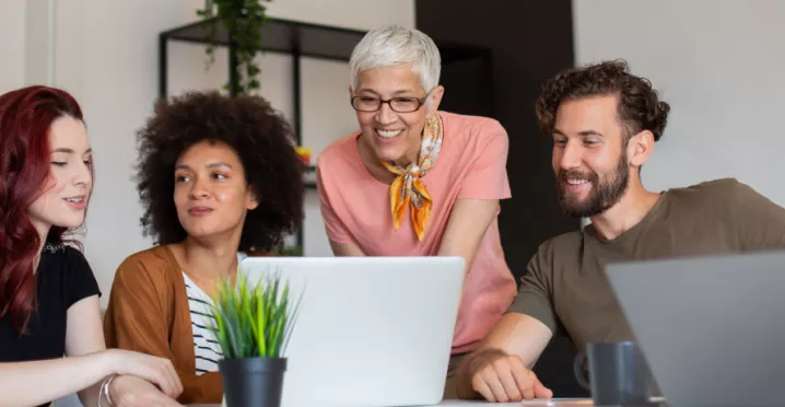 Four employees in varying generations working together at a computer at work.