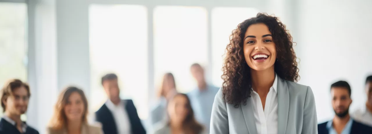 Shows a woman smiling at the camera with colleagues behind her