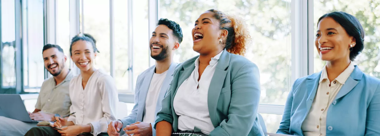 Five employees sitting down laughing on a couch together