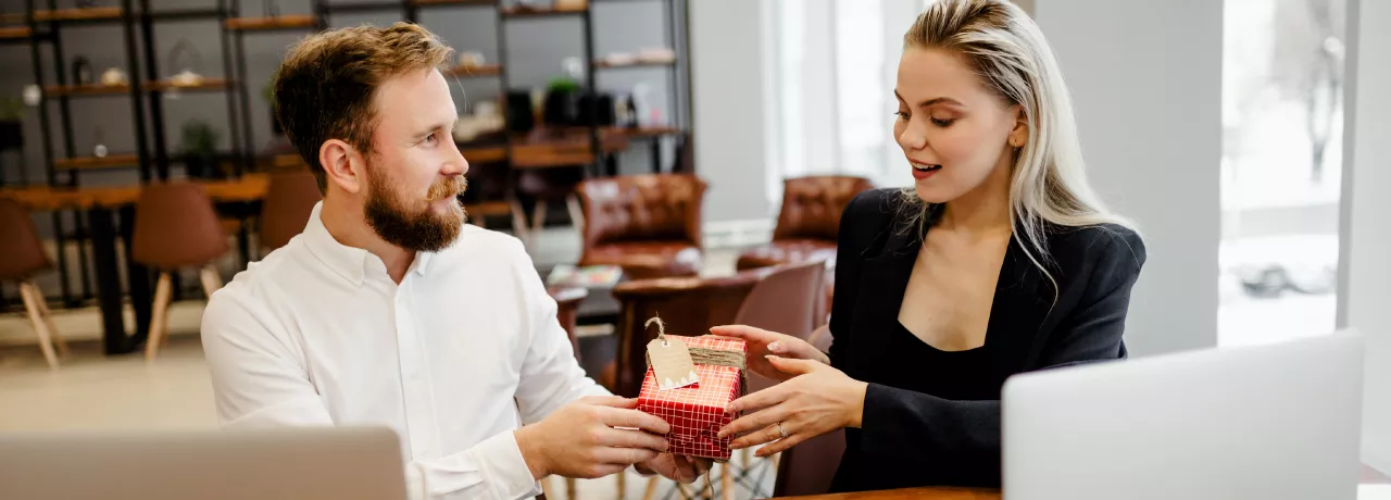 Image shows one employee giving a gift to another employee.