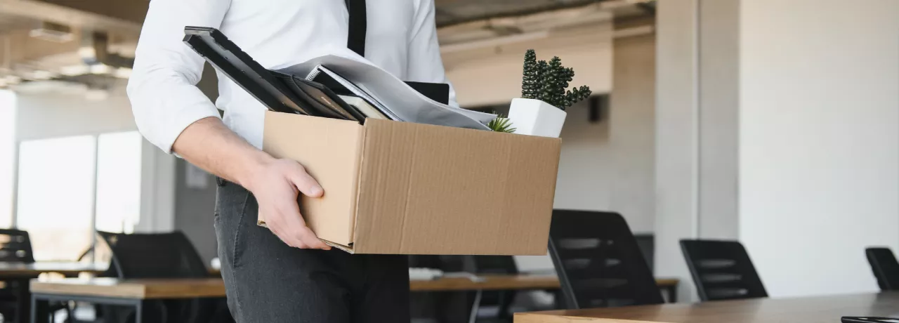 Image shows a person leaving an office with a box of items.