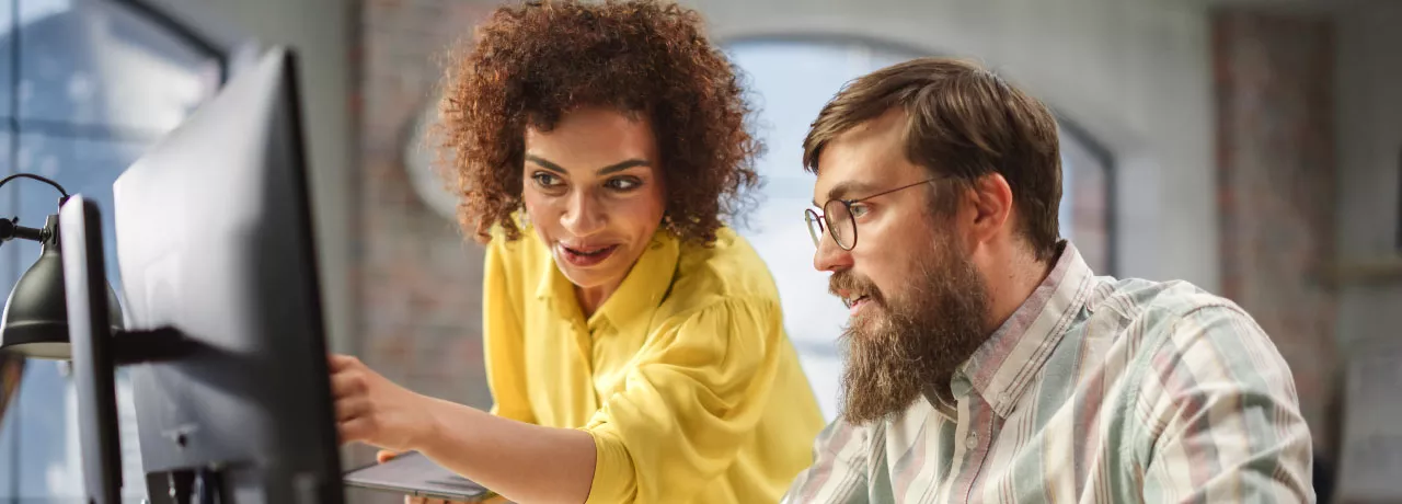 An employee training a new hire in front of a computer as part of their onboarding strategy