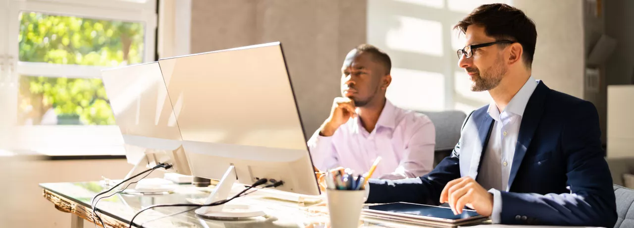 Two employees happily looking at a computer screen at their desk