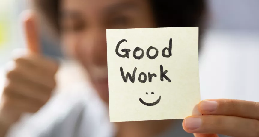 A woman holding a sticky note that says "Good work" with a smiley face