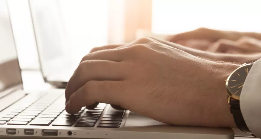 Image shows a close up of a person typing on their laptop