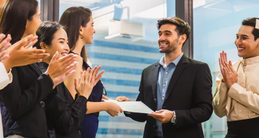 Image shows an employee receiving a certificate in front of a group of employees.