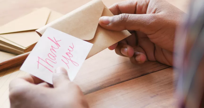 Image shows a person putting a note that says "thank you" into an envelope