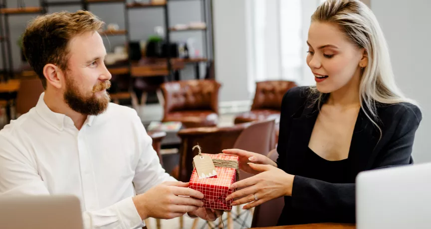Image shows one employee giving a gift to another employee.