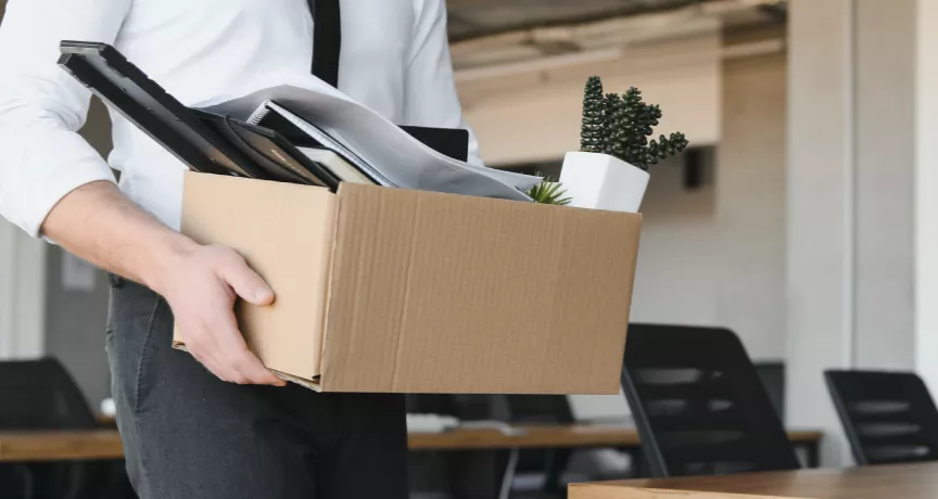Image shows a person leaving an office with a box of items.