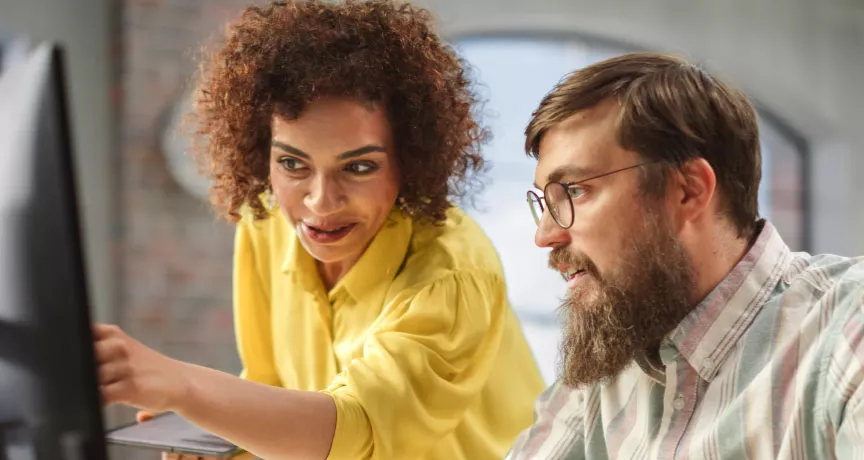 An employee training a new hire in front of a computer as part of their onboarding strategy