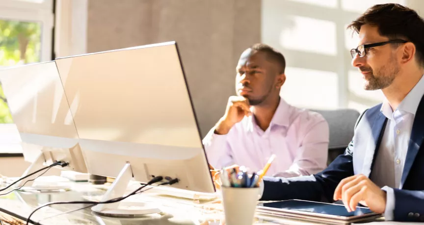 Two employees happily looking at a computer screen at their desk