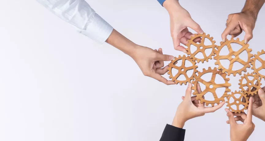 A group of employees creating a cogwheel with each holding a small cog