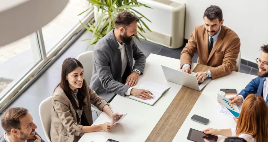An image of a leadership team going over ways to create a healthy company culture and positive work culture to recognize employees and contribute to business success. They are discussing team building activities to integrate new employees into the organization's culture to create a positive environment and overall thriving culture.