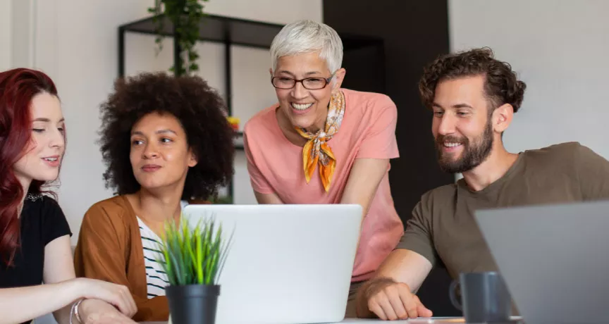 Four employees in varying generations working together at a computer at work.