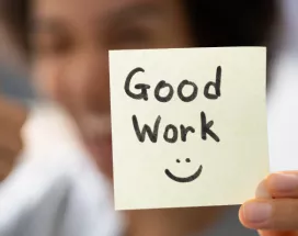 A woman holding a sticky note that says "Good work" with a smiley face