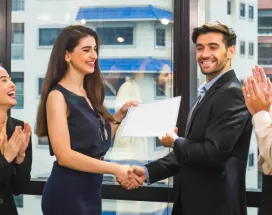 Image shows a coworker presenting an award to another coworker in front of a group of teammates.