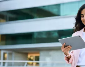 A woman in business clothes smiling down at her tablet