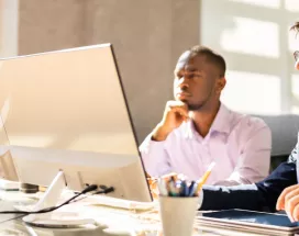 Two employees happily looking at a computer screen at their desk