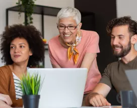 Four employees in varying generations working together at a computer at work.