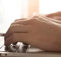 Image shows a close up of a person typing on their laptop