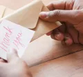 Image shows a person putting a note that says "thank you" into an envelope