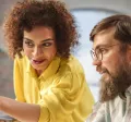 An employee training a new hire in front of a computer as part of their onboarding strategy