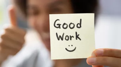 A woman holding a sticky note that says "Good work" with a smiley face