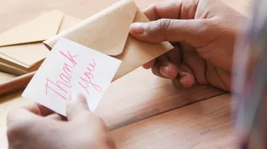 Image shows a person putting a note that says "thank you" into an envelope