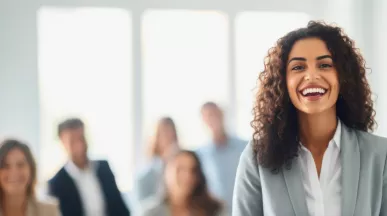 Shows a woman smiling at the camera with colleagues behind her