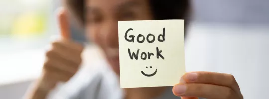 A woman holding a sticky note that says "Good work" with a smiley face