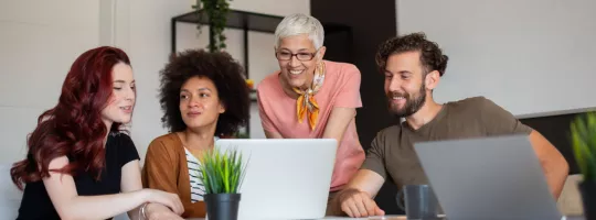 Four employees in varying generations working together at a computer at work.